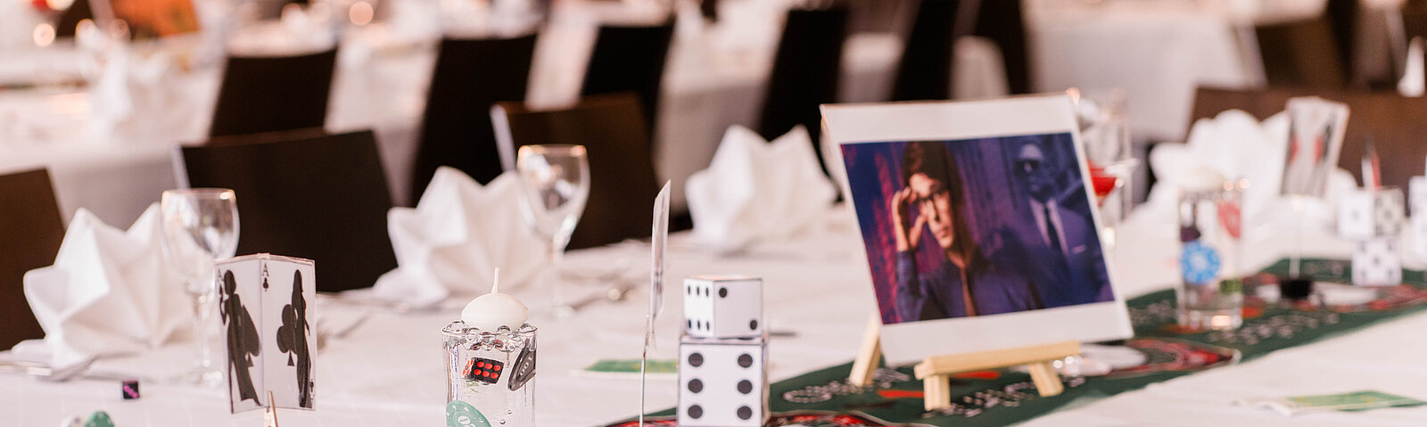 Nahaufnahme einer festlich gedeckten Tafel mit weißen Tischdecken, Stoffservietten und Dekoration im Spielcasino-Thema.